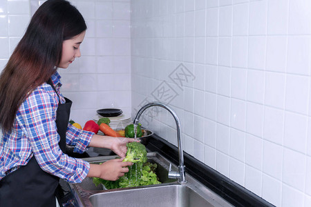 年轻女子用厨房的供水槽清洗蔬菜图片