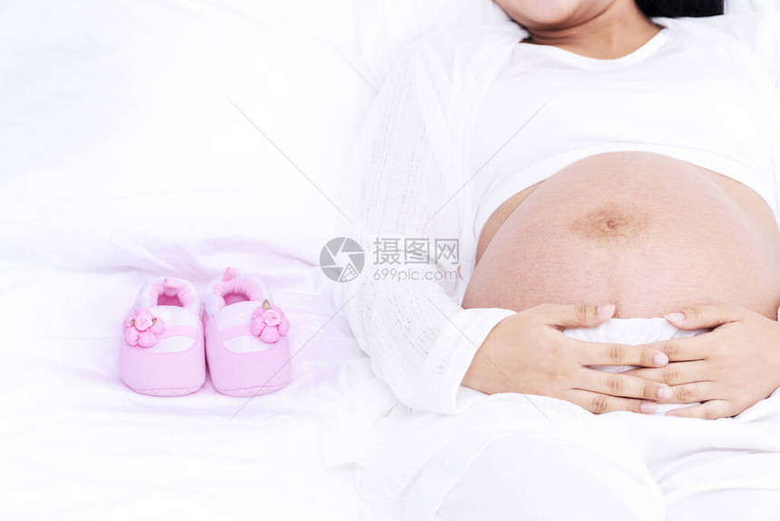 怀孕的年轻妇女躺在白床上图片