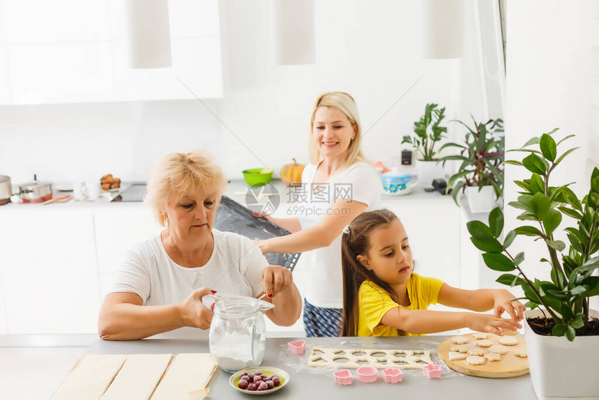 小女孩与母亲和祖母一起学习卷钱做自制糕点或饼干图片