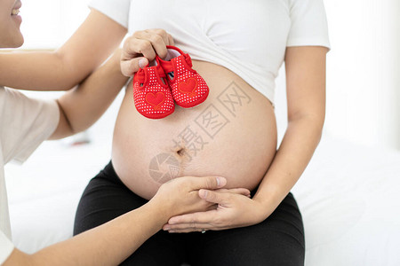 亚洲种族快乐的孕妇在她的大肚子上展示了一只红色的婴儿鞋图片