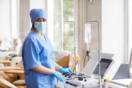 戴着口罩和制服的护士在医院使用献血医疗设备时看图片