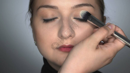 化妆师在美容工作室为年轻女子制作专业化妆化妆师用刷子在眼睑上涂抹腮红图片