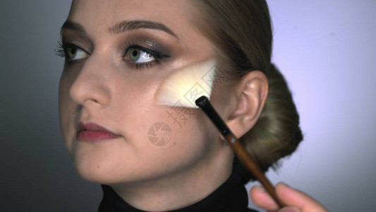 化妆师在美容工作室为年轻女子制作专业化妆化妆师使用刷子涂抹闪光图片