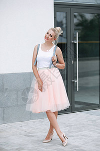 金发女人在城市的街道上摆姿势时尚的衣服看粉色裙子白衬图片