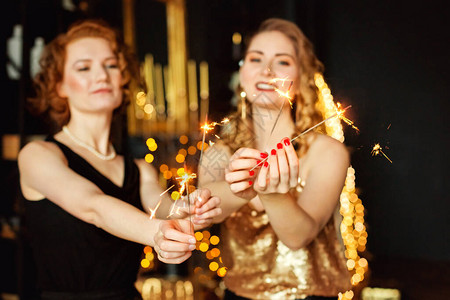 选择焦点两个美丽的散景女人圣诞花环和礼物手中的烟火金色圣诞装图片