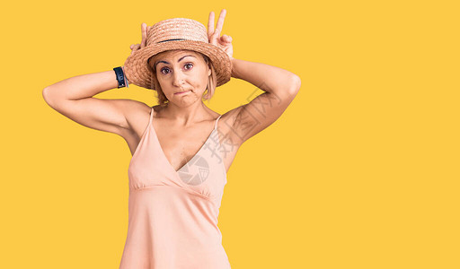 穿着暑假帽子的金发年轻女人手掌用耳朵做手势看上去冷嘲热讽图片