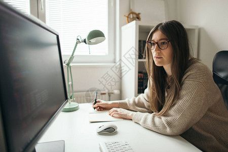 专注于在台式电脑上工作的年轻女在她的家庭办公室用电脑工作图片