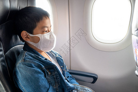 亚洲男孩戴面罩坐在飞机舱窗户附近的客背景图片