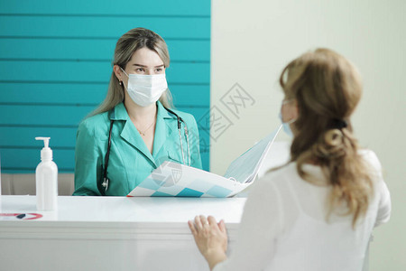 一名戴医疗面具的女医生或护士在医院候诊室与一名女病人交谈在手图片