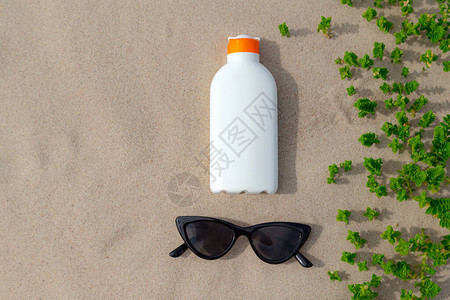 阳光明媚的日子在沙滩上的防晒霜和太阳镜白色防晒霜保护瓶免受图片