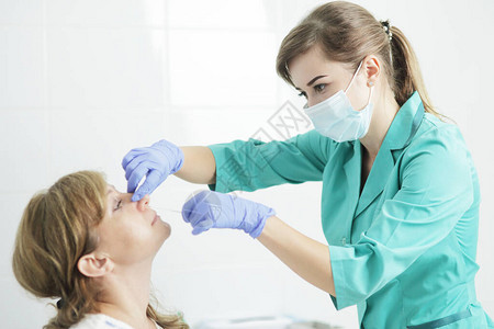 一名身戴医疗面具的护士从病人鼻子上抽取一个擦拭剂图片