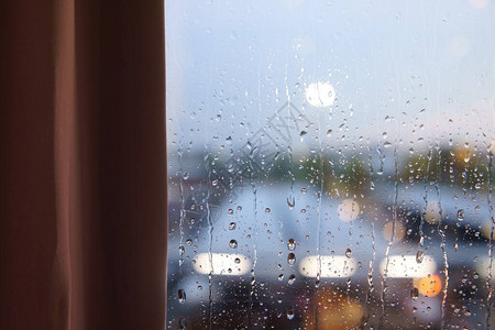 或房间的暴雨棕色窗帘透明玻璃窗上的水滴和街道上的办公城图片