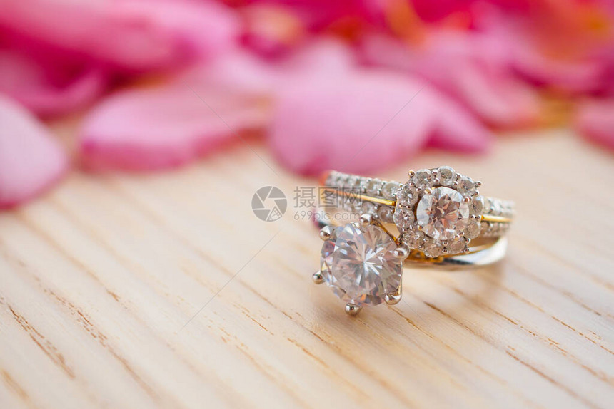 木桌上的钻石结婚戒指美丽的粉红玫瑰花瓣背图片