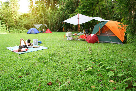 在丛林花园或森林的绿草地上与薄布和树下儿童家庭搭建自然景观帐篷图片