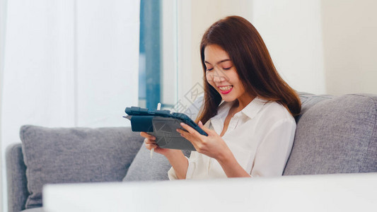 年轻亚洲商业女使用平板视频电话在客厅工作时与家人交谈图片