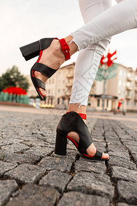 穿着复古牛仔裤穿着优雅的红色和黑色凉鞋的时尚女孩站在城市一条石路图片