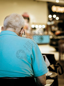 老年男顾客在咖啡店排队等候外卖饮料时使用智能手机的背影新常态的图片