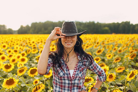向日葵田里戴着牛仔帽格子衬衫和牛仔裤的年轻女农艺图片