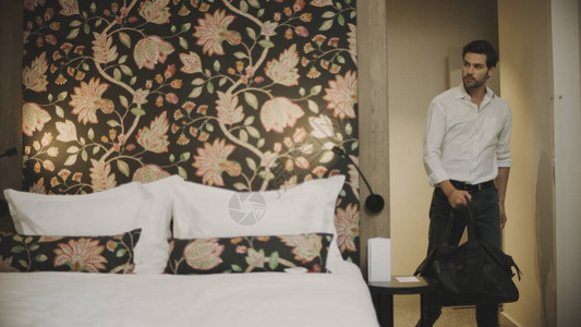 生意人进入豪华酒店房间快乐男人在卧室里跳床喜悦的家伙带着旅行袋图片