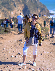 妇女旅行白裤子黄色皮夹克太阳镜站在海洋边的妇女图片