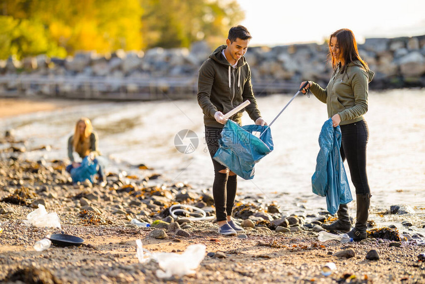 女人把垃圾放在海滩上男人拿着的袋子里社区志愿者团队在阳光明媚的日子打扫卫生他们图片