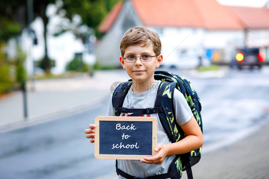 戴着眼镜和背包或书包的快乐小男孩在去初中或高中的路上的小学生户外街上的孩子回到学校拿着图片