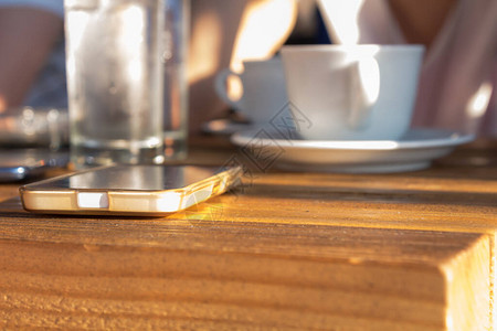 咖啡店桌上的现代手机背景上的人模糊不图片