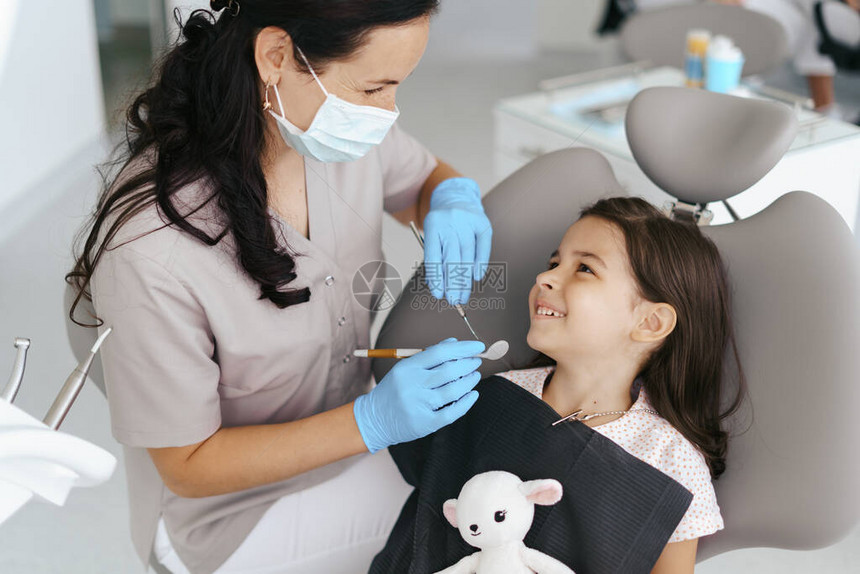 可爱的小女孩坐在现代牙科椅上与牙医图片