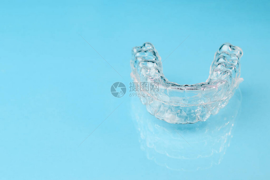 在蓝色背景和复制空间上关闭看不见的连接器塑料牙套将牙科保留员固定在图片