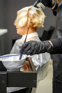 穿黑手套的发型师在理发沙龙中白色年轻女子染发图片