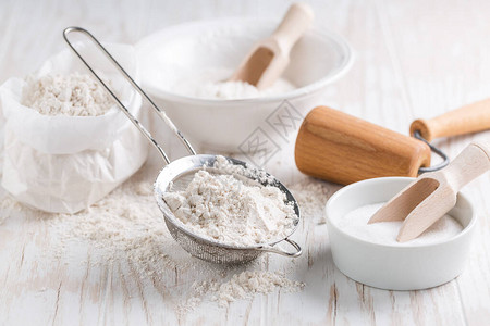 在白色木桌上拼写面粉糖和烘焙原料和厨房用具图片