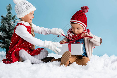 身戴帽子和冬季服装的儿童坐在雪上图片