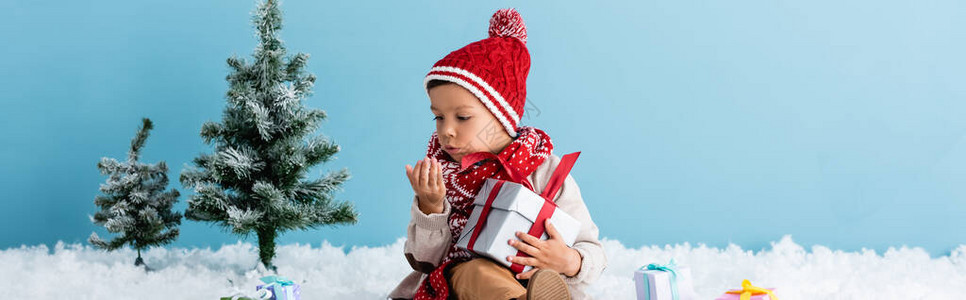 穿着帽子和冬季服装的男孩坐在雪上图片