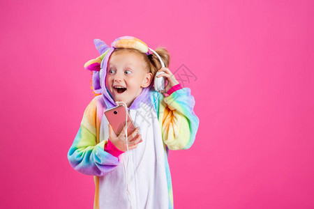 穿着独角兽制服的快乐金发女孩从她的智能手机里听音乐在粉红背景和文字图片