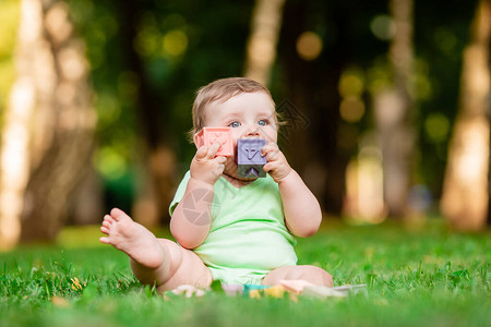 夏天穿着绿色紧身衣裤的可爱孩子坐在草地上玩发育玩具儿童发展长图片