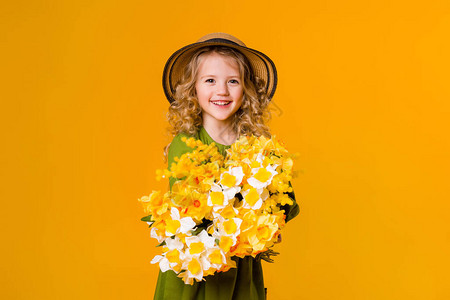 穿着绿色亚麻连衣裙和黄色橡胶靴的快乐女孩拿着一束鲜花在黄色背景上图片