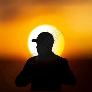 日落太阳背景下戴棒球帽的旅行者剪影图片