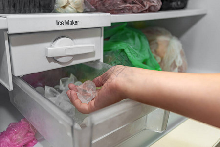 女孩从冰箱的制冰机里取冰块来冷却背景图片