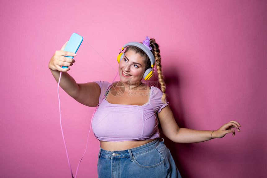 年轻漂亮的大码女在粉红色背景下自拍孤立的胖乎的年轻女戴着耳机工作室拍摄直播社交网络女孩力量图片