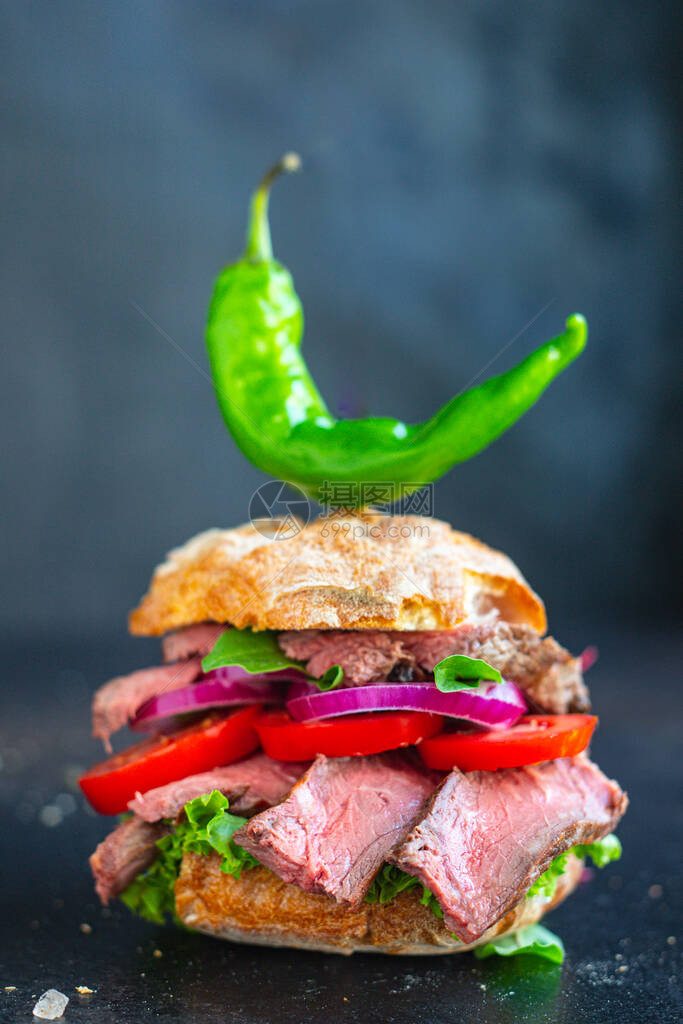 餐桌上含有面包番茄生菜中型或稀有牛排的肉和蔬菜面包三明治图片