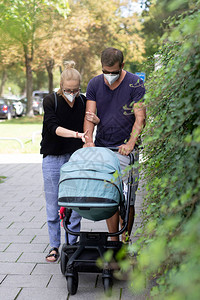 担心的年轻父母带着戴医用口罩的婴儿车走在空荡的街道上图片