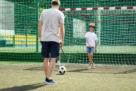 两个男人一起踢足球的肖像站在球门前等球的小男孩图片