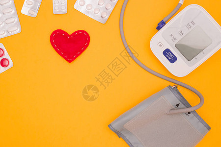 健康心脏病学血压的概念黄色背景上的血压监测仪药丸和组织心脏顶视图图片