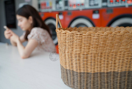 亚洲女用智能手机在现代洗衣机自助洗衣店等着她的衣服图片
