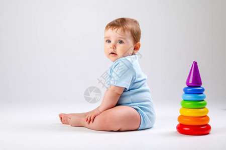 蓝色体衣中可爱的婴儿与多色金字塔玩耍白色背景图片