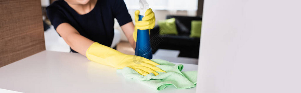 戴橡皮手套的女佣在清扫旅馆房间的架子时携带喷洒瓶和抹图片