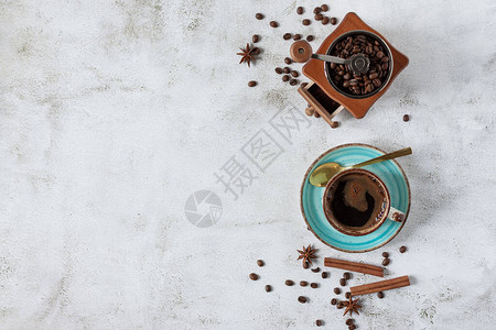 一杯带有肉桂茴香料和老式咖啡研磨机顶视图的咖啡灰色背景的咖啡杯和豆子图片