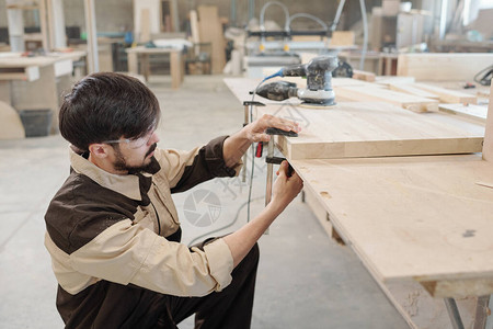 工作服和防护眼镜的年轻男工使用工作台加工木图片