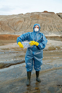 身着防护服呼吸器橡胶手套和靴子的年轻女科学家拿着装有水和土壤样图片