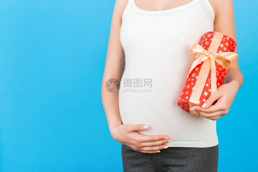 穿着家庭服装的孕妇在蓝背景上拿着礼物盒的近身肖像庆祝妊娠图片